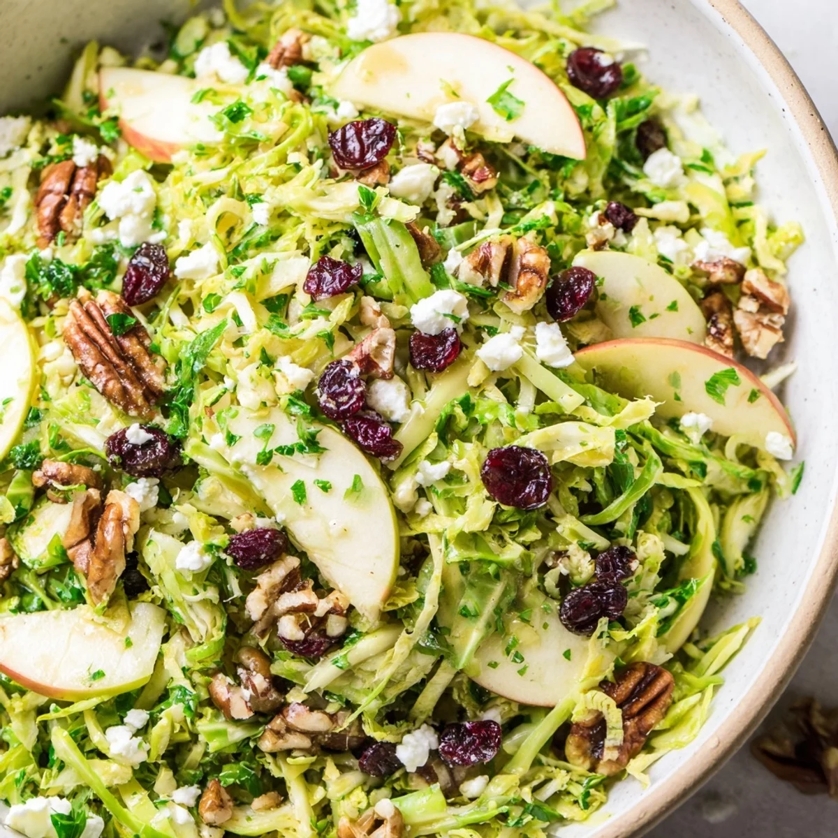 Shaved Brussels sprout apple salad bowl with maple Dijon dressing in white serving dish