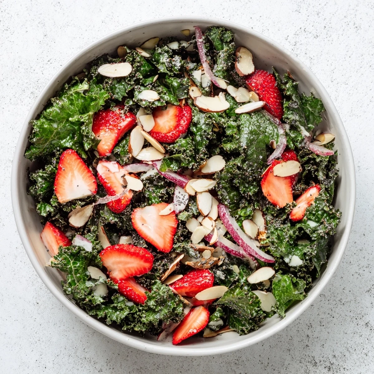 Colorful crispy kale strawberry almond salad bowl drizzled with creamy poppyseed dressing