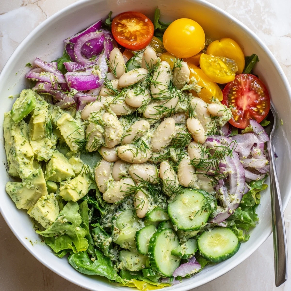 Protein-packed dill avocado white bean salad in a bowl with colorful mixed greens and tomatoes