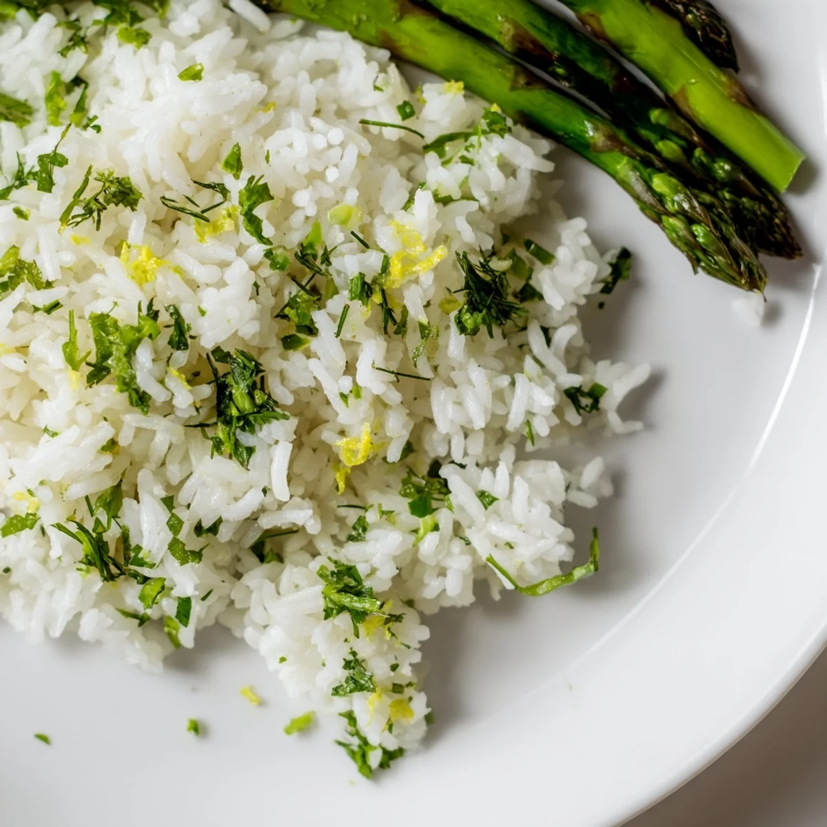 Fluffy lemon herb Jasmine rice served alongside charred grilled asparagus spears on a white plate