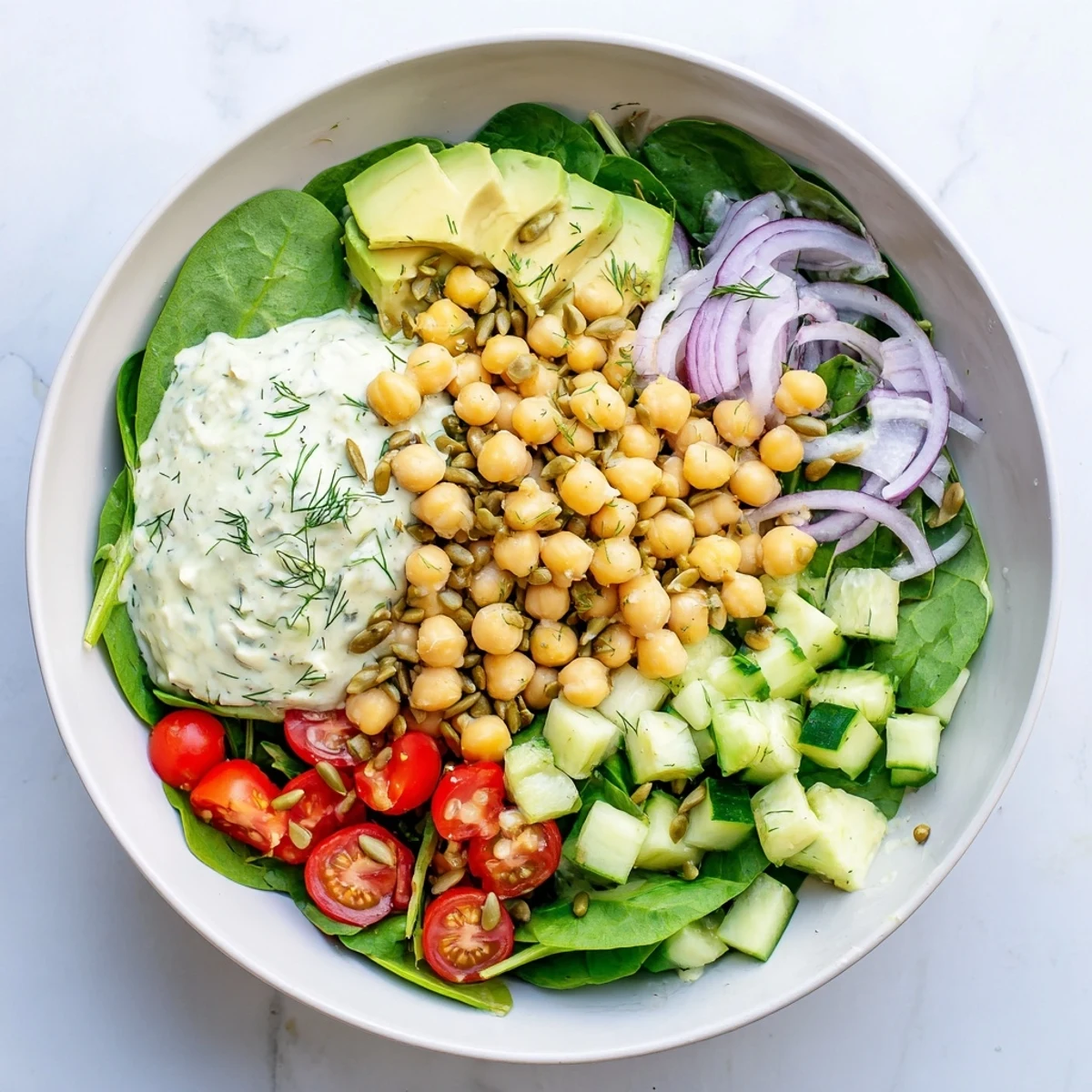 Creamy avocado spinach chickpea salad bowl topped with toasted sunflower seeds and fresh dill dressing