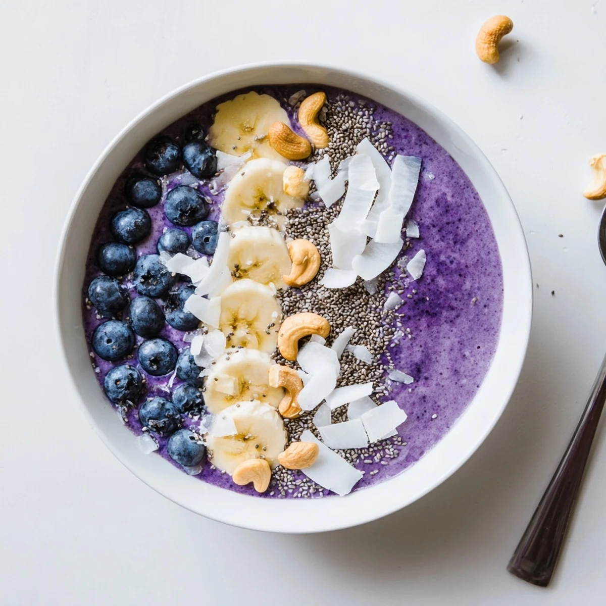 Thick blueberry vanilla cashew smoothie bowl topped with fresh berries, chia seeds and chopped nuts