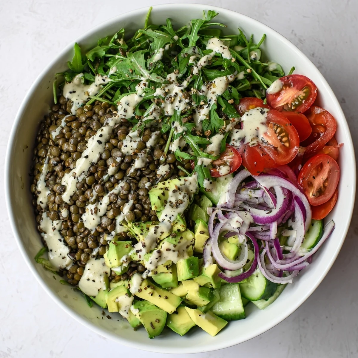 Colorful creamy avocado arugula lentil salad bowl drizzled with tangy lemon-tahini dressing and sprinkled with crunchy hemp seeds