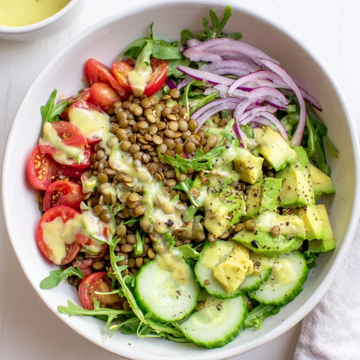 Vibrant plant-based salad bowl packed with creamy avocado, peppery arugula, tender lentils, and zesty tahini dressing