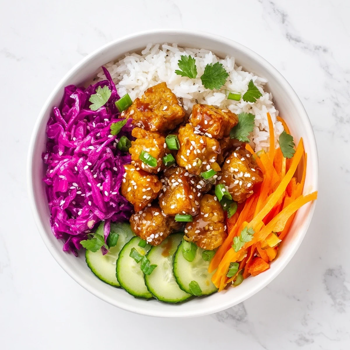 Asian-inspired vegan bowl featuring sticky glazed tempeh with pickled red cabbage, julienned carrots, fresh coriander, and toasted sesame seeds over steamed rice