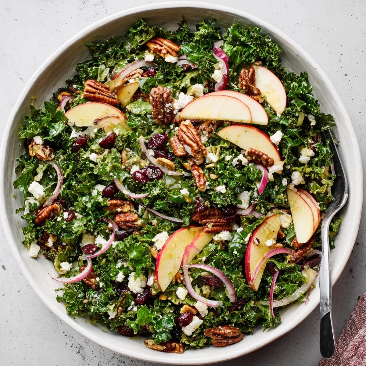 Fresh kale salad bowl topped with crisp apples and toasted pecans in maple dressing