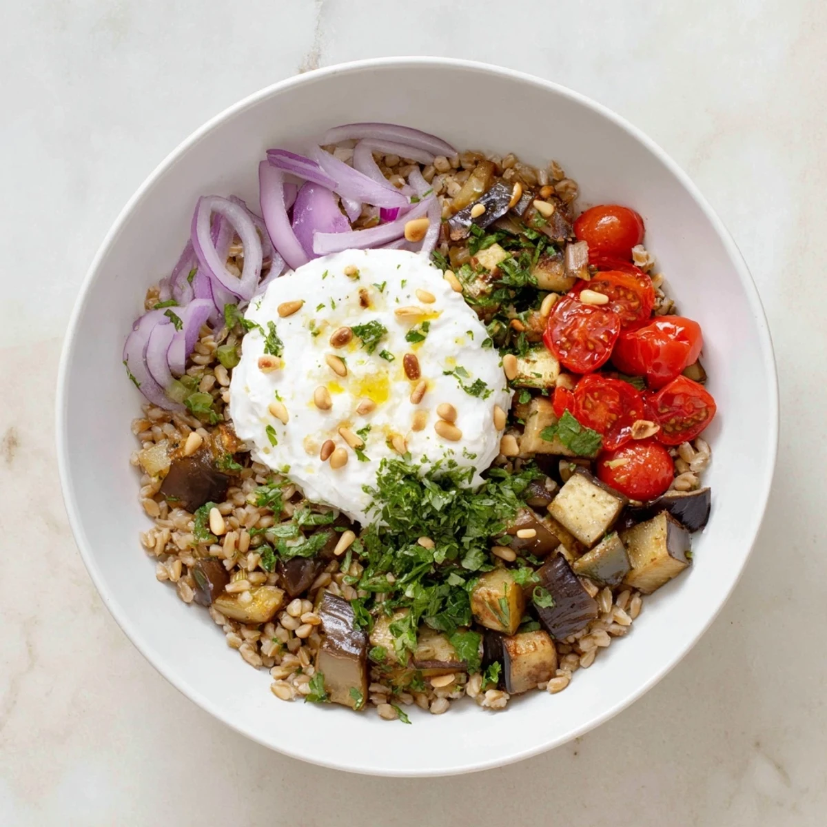 Golden roasted eggplant and vegetables mounded over fluffy farro in a Mediterranean herb grain bowl