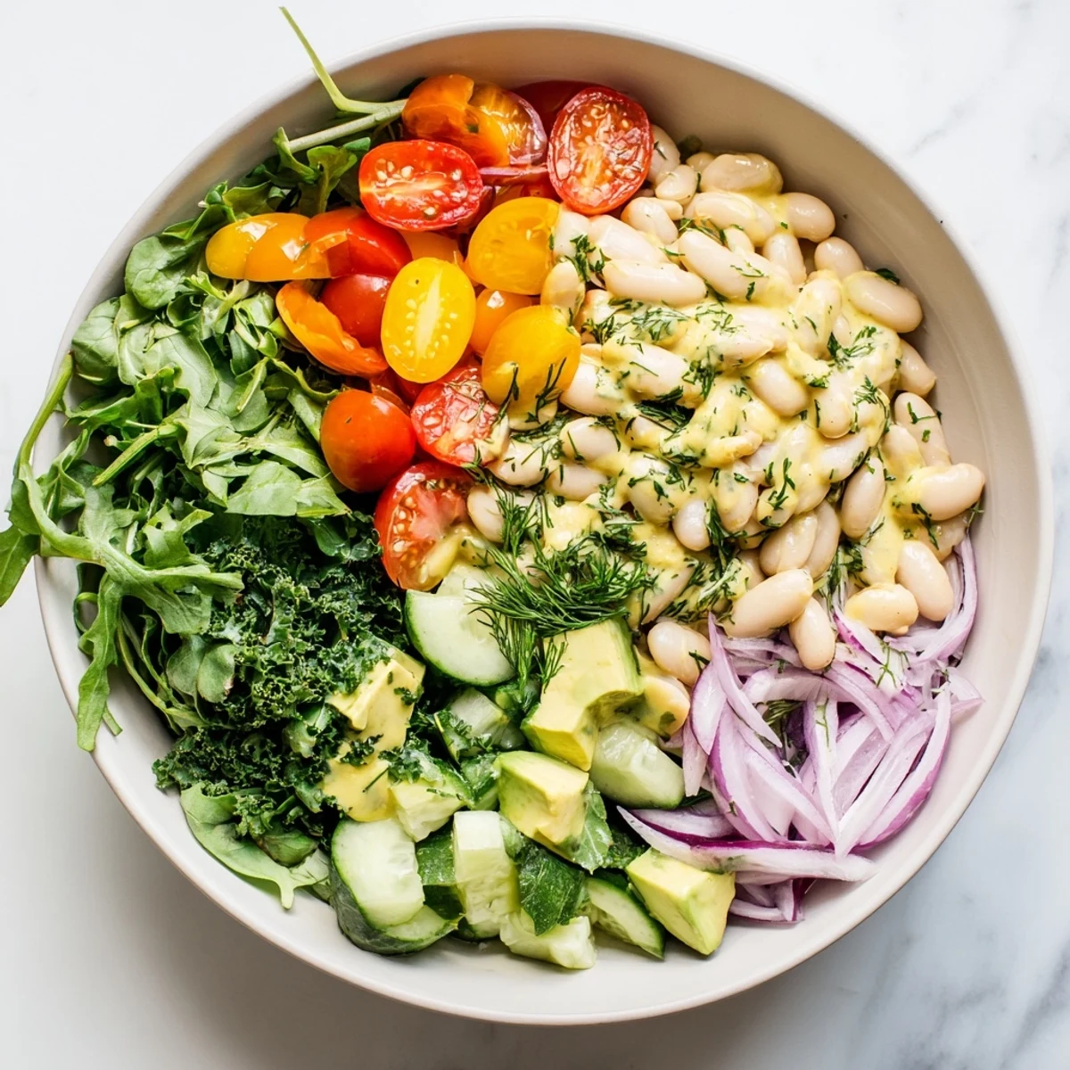 Colorful creamy lemon avocado white bean salad bowl topped with fresh herbs and crisp vegetables