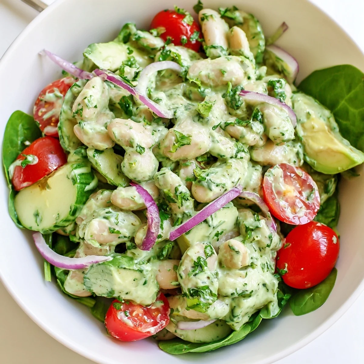 Vibrant bowl of white bean salad with fresh cucumbers and creamy green goddess dressing garnished with chopped herbs and avocado
