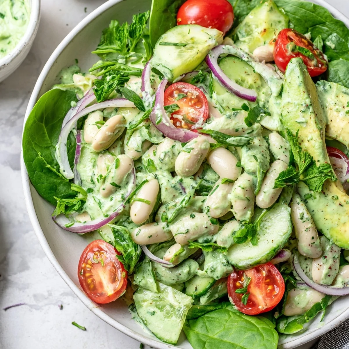 Fresh white bean salad bowl featuring crunchy cucumbers and smooth green goddess dressing on a bed of baby spinach