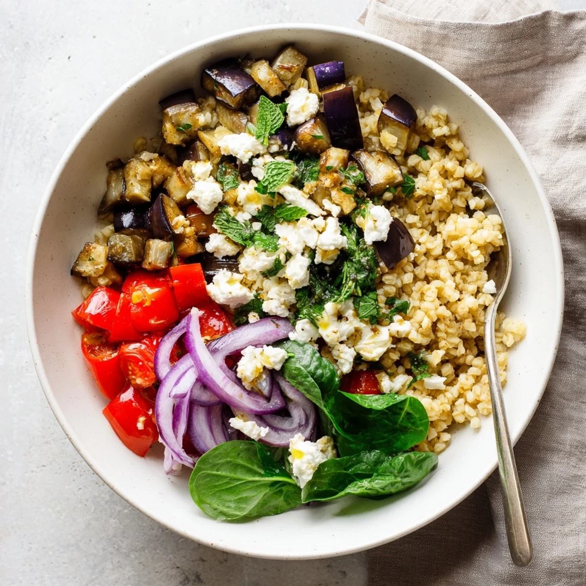 Colorful Mediterranean roasted eggplant bulgur grain bowl topped with crumbled feta cheese