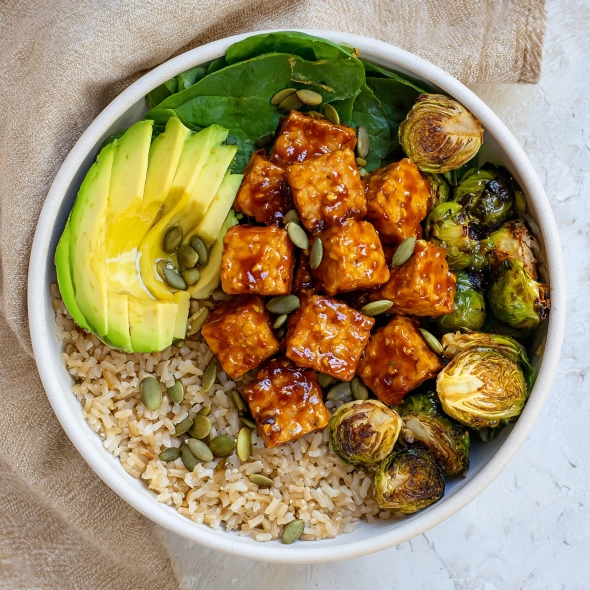 Vegan power bowl featuring maple glazed tempeh alongside crispy roasted Brussels sprouts over a bed of grains