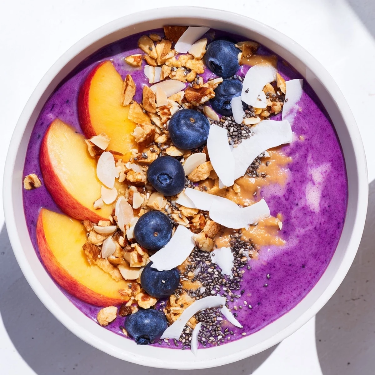 Thick creamy smoothie bowl featuring blueberries, peaches, and almond butter with granola crumble