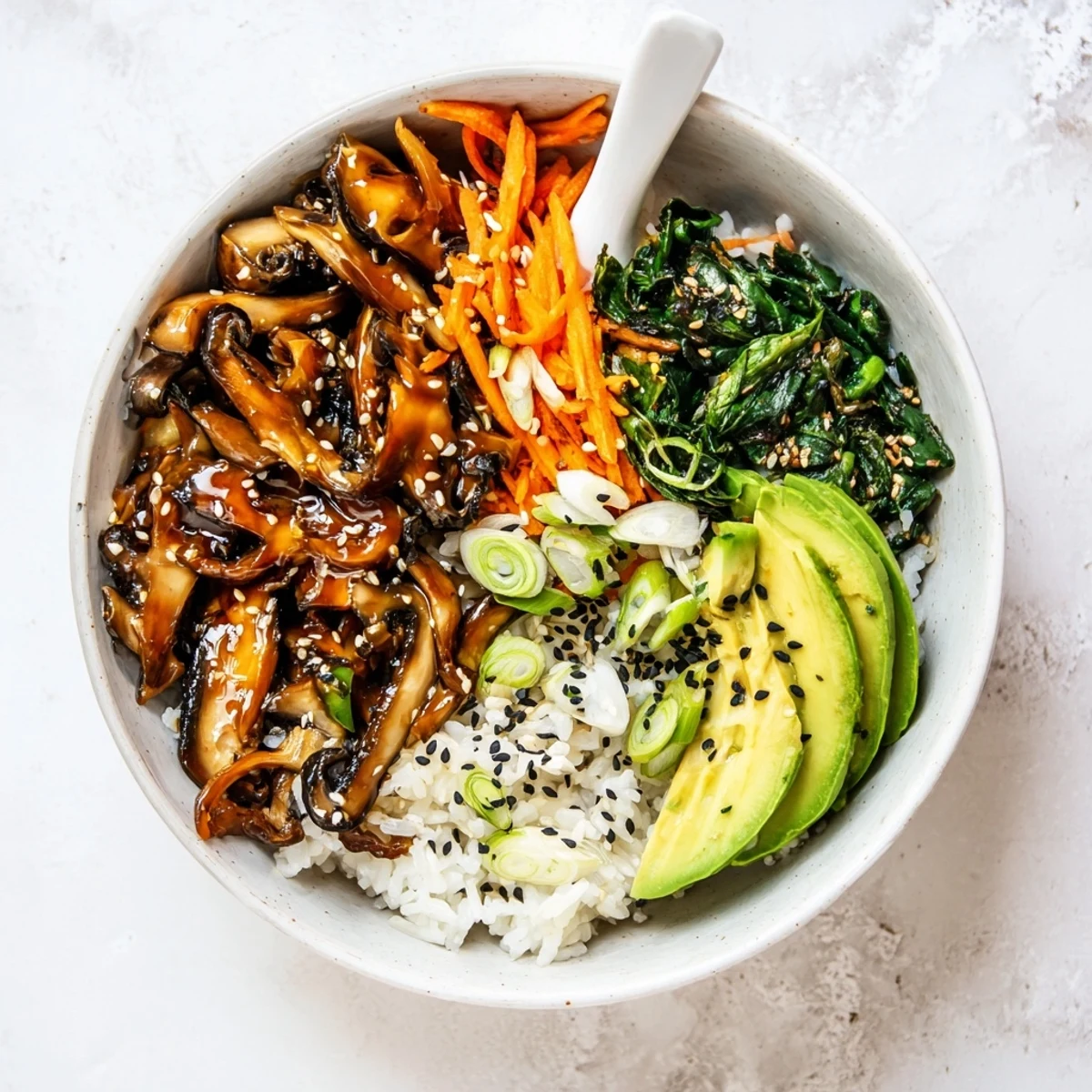 Colorful teriyaki mushroom bowl with wilted sesame greens, carrot, and avocado slices over rice