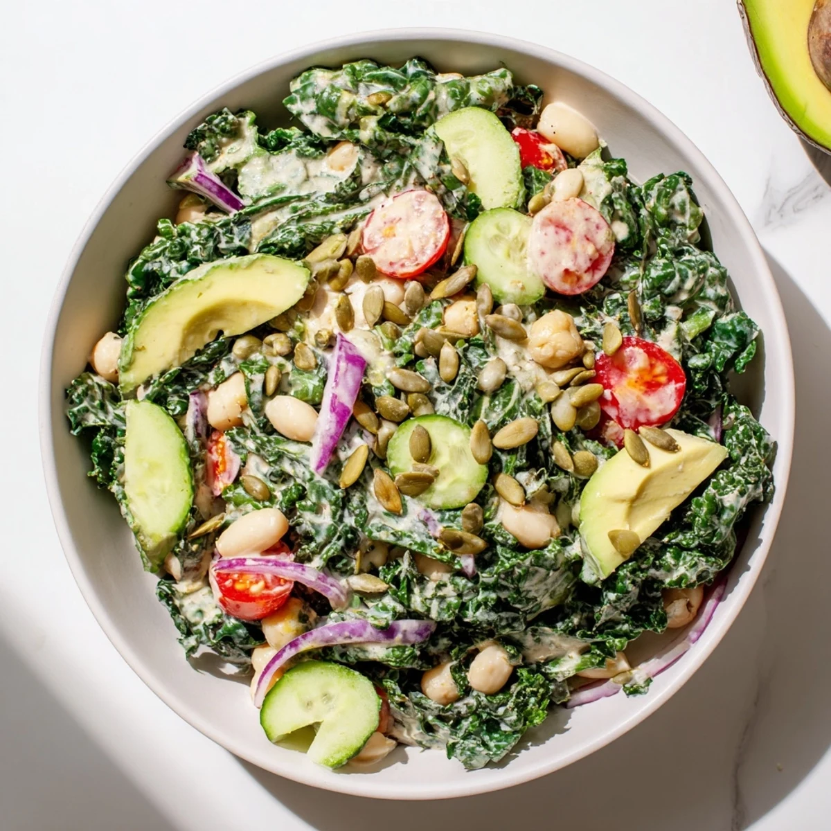 Colorful vegan salad bowl featuring massaged kale, white beans, creamy lemon tahini dressing, and toasted seed crunch