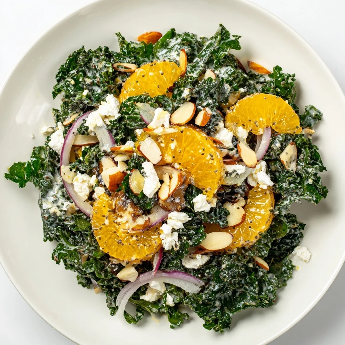 Shaved kale citrus almond salad bowl drizzled with creamy poppyseed dressing on white plate