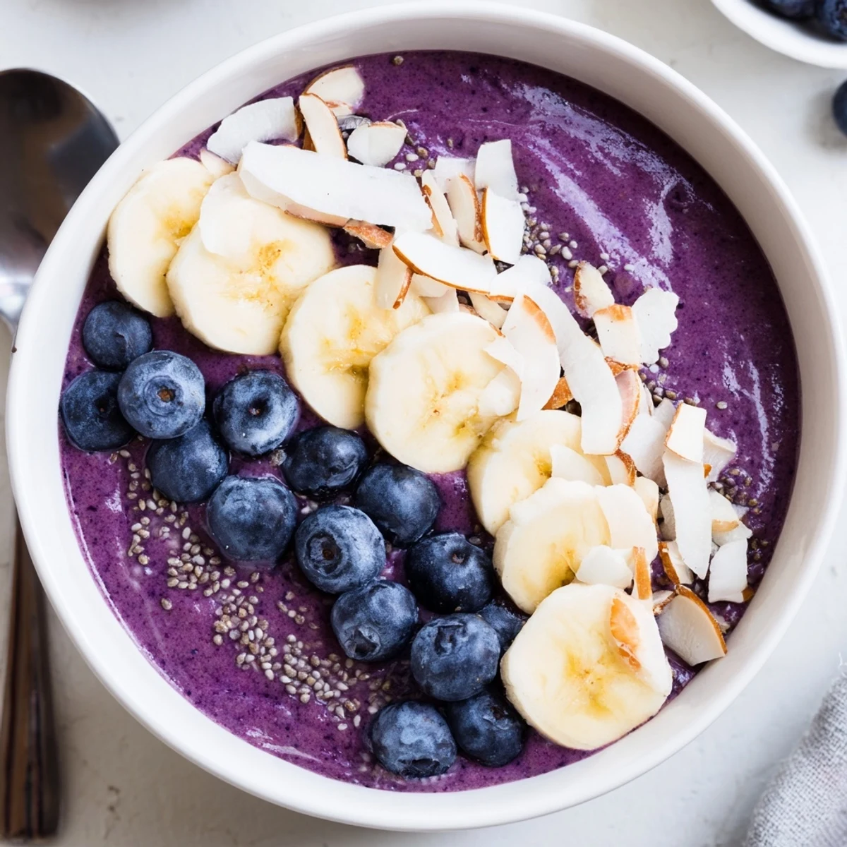Purple blueberry banana almond smoothie bowl topped with coconut flakes, fresh berries, and sliced almonds
