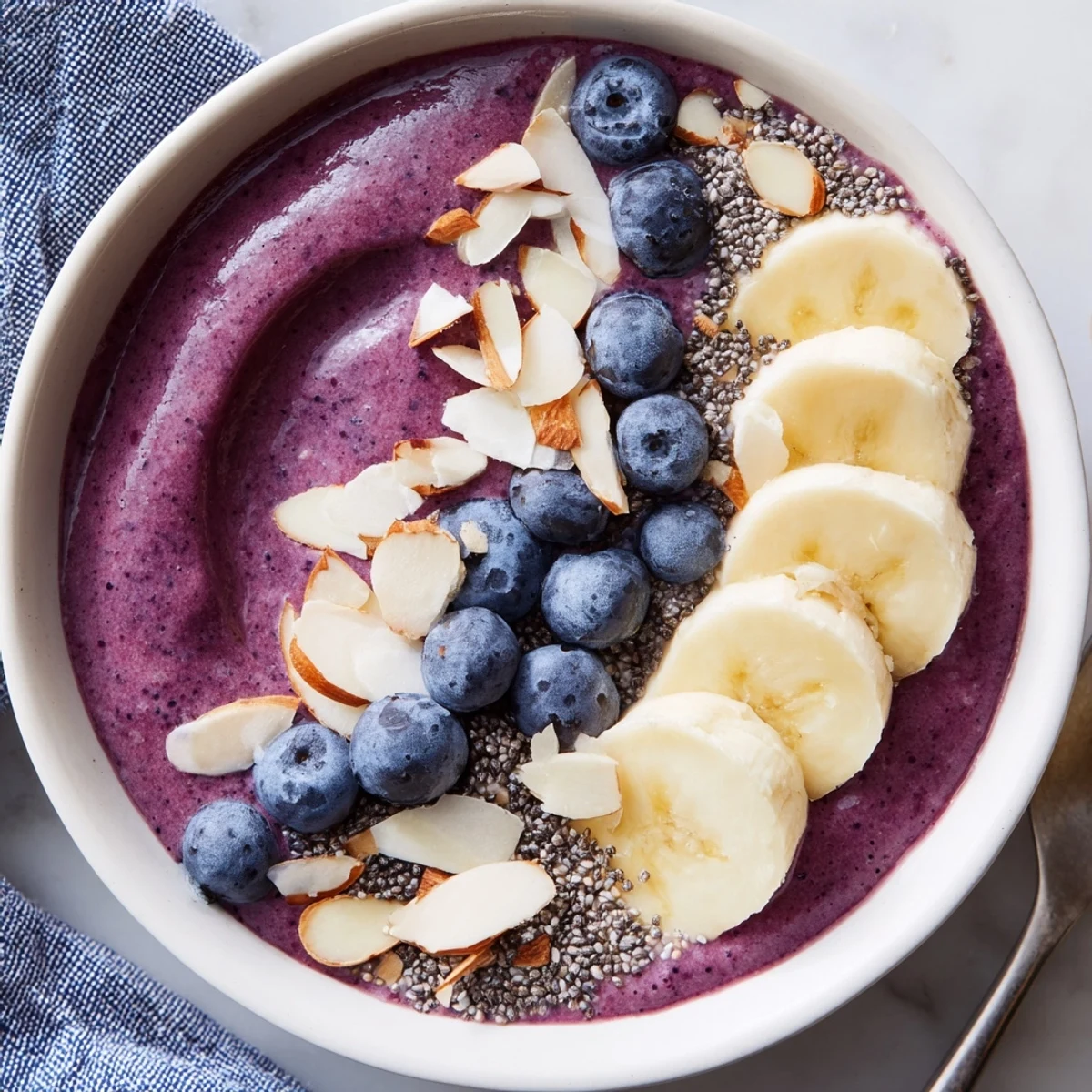 Creamy blueberry banana almond smoothie bowl drizzled with honey and sprinkled with crunchy coconut flakes