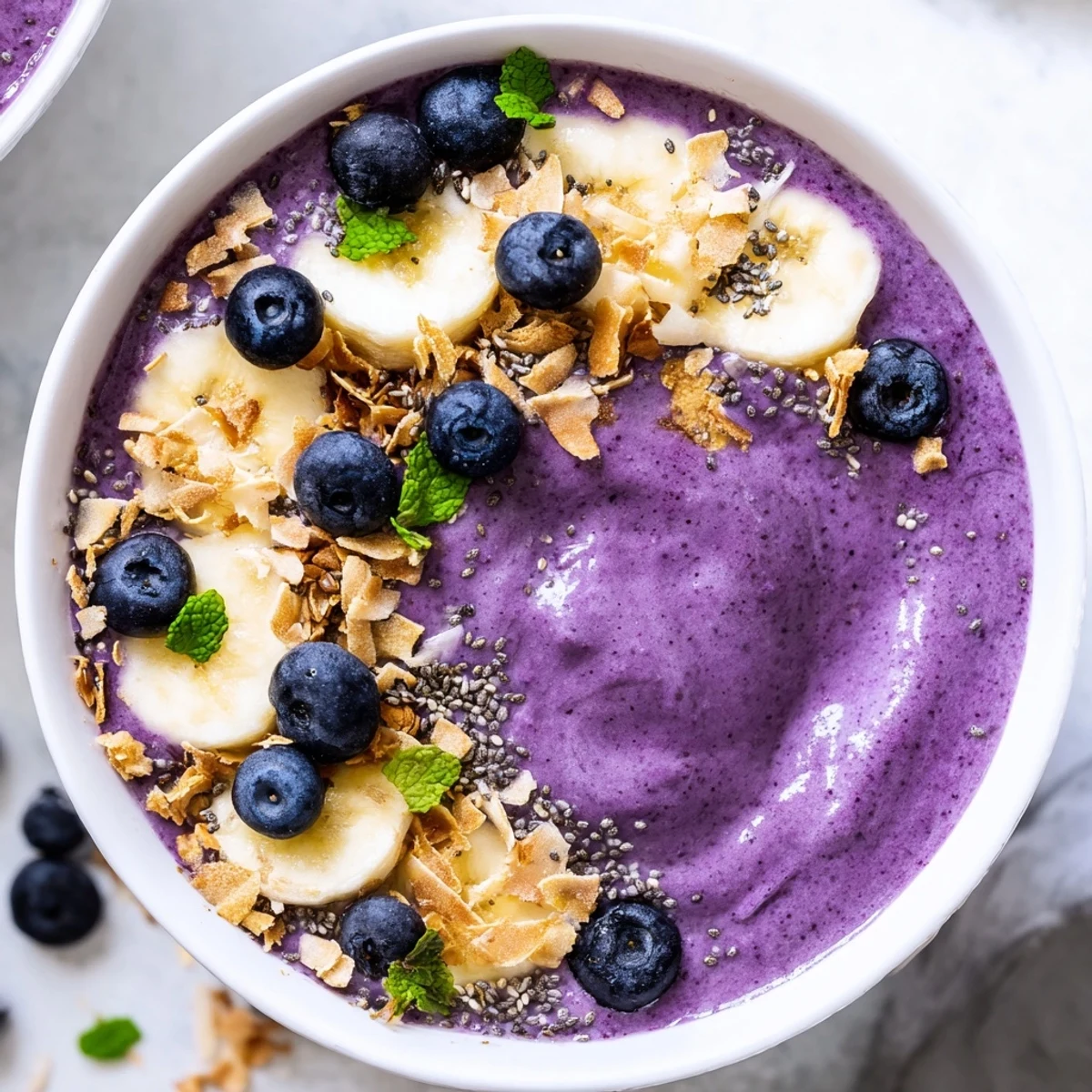 Purple blueberry coconut chia smoothie bowl topped with fresh berries and crunchy toasted coconut flakes