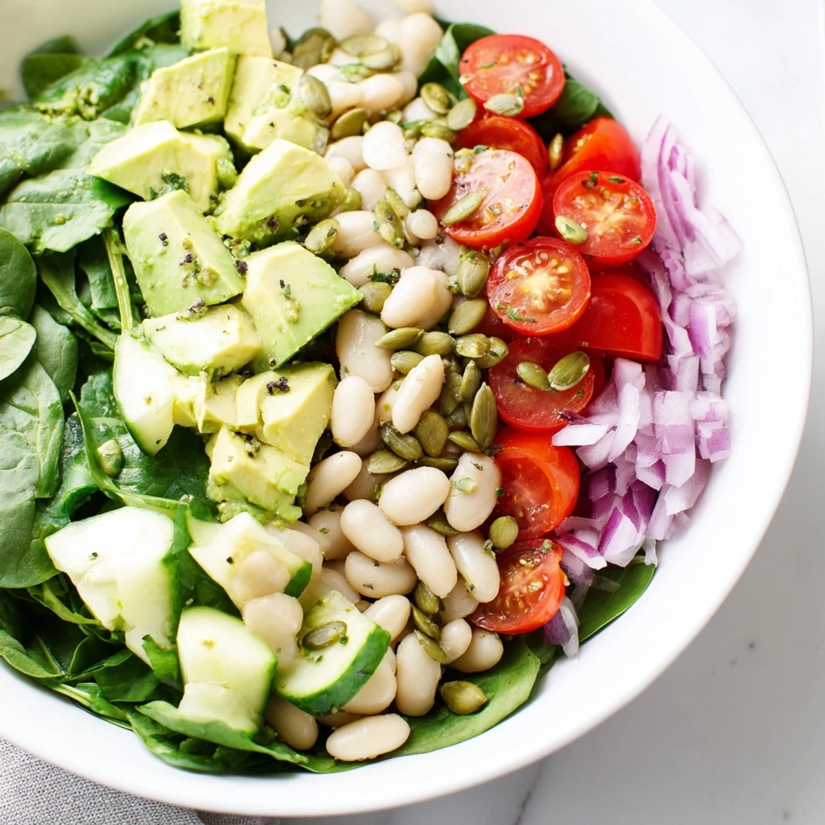 Fresh spinach leaves tossed with creamy avocado, tender white beans, and bright citrus dressing in rustic bowl