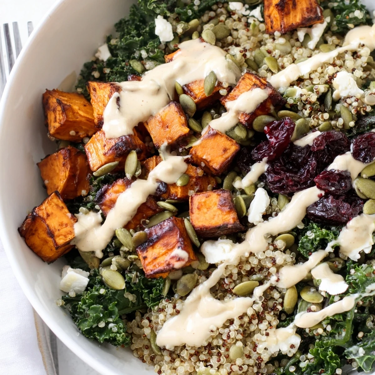 Warm roasted sweet potatoes nestled over fluffy quinoa and massaged kale in this vibrant grain bowl finished with maple tahini.
