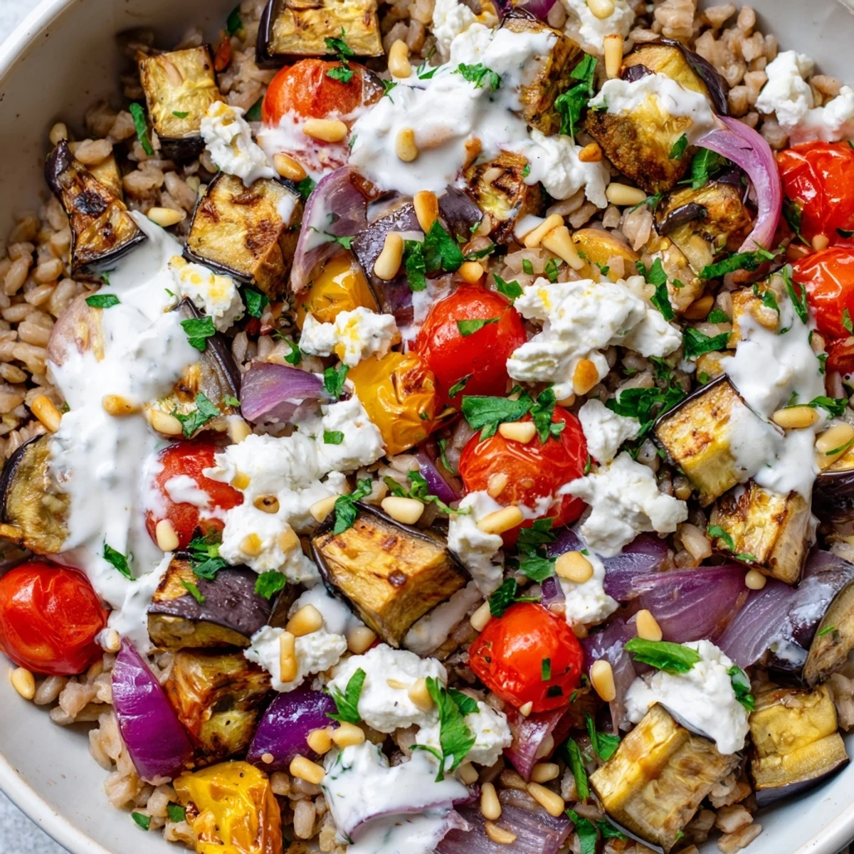 Mediterranean roasted eggplant farro grain bowl topped with creamy yogurt sauce and fresh vegetables