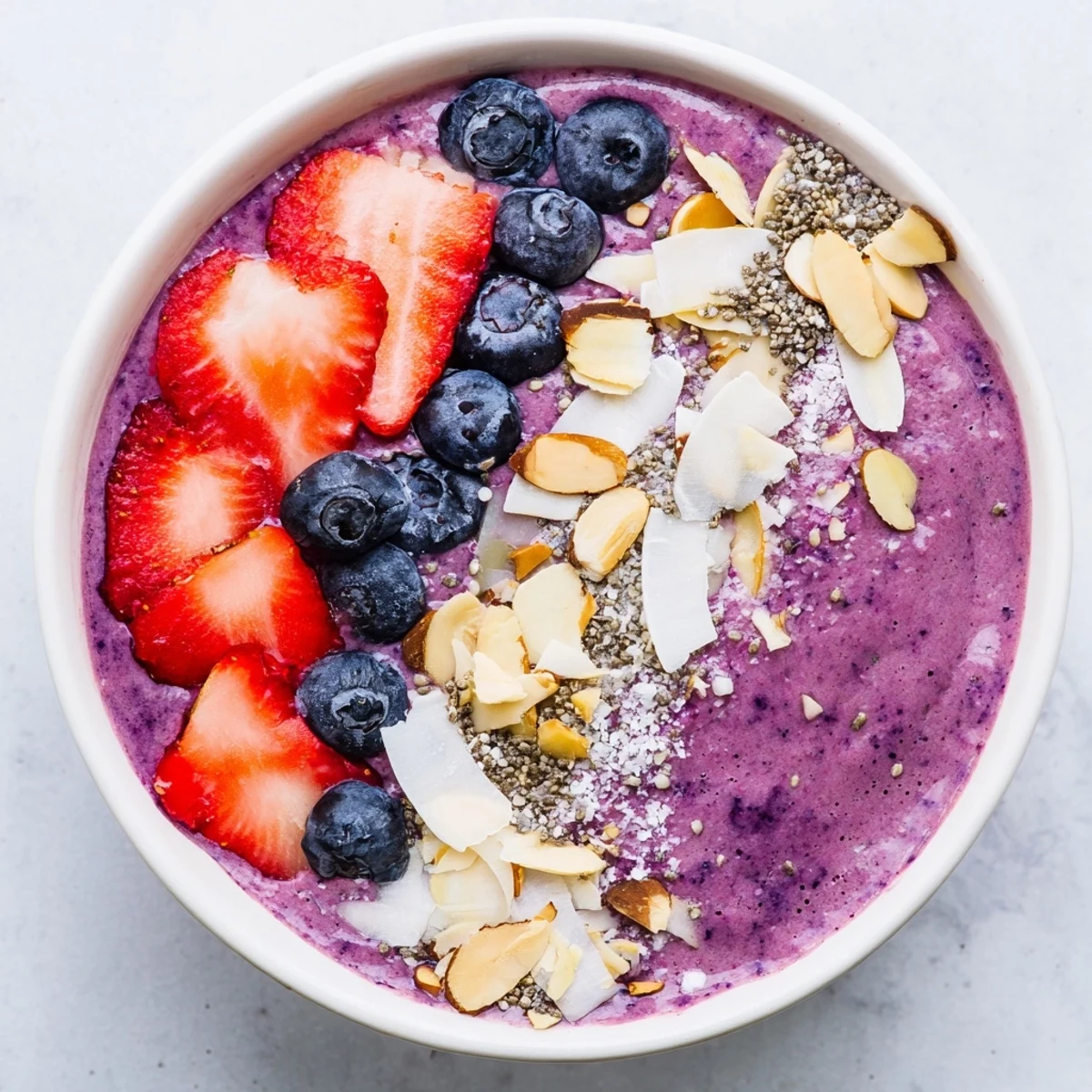 Creamy blueberry strawberry almond smoothie bowl drizzled with honey and crunchy toppings arranged neatly