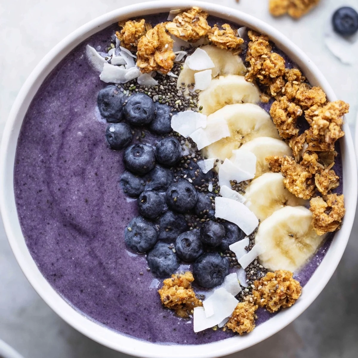 Creamy blueberry coconut banana smoothie bowl topped with crunchy granola clusters and fresh fruit