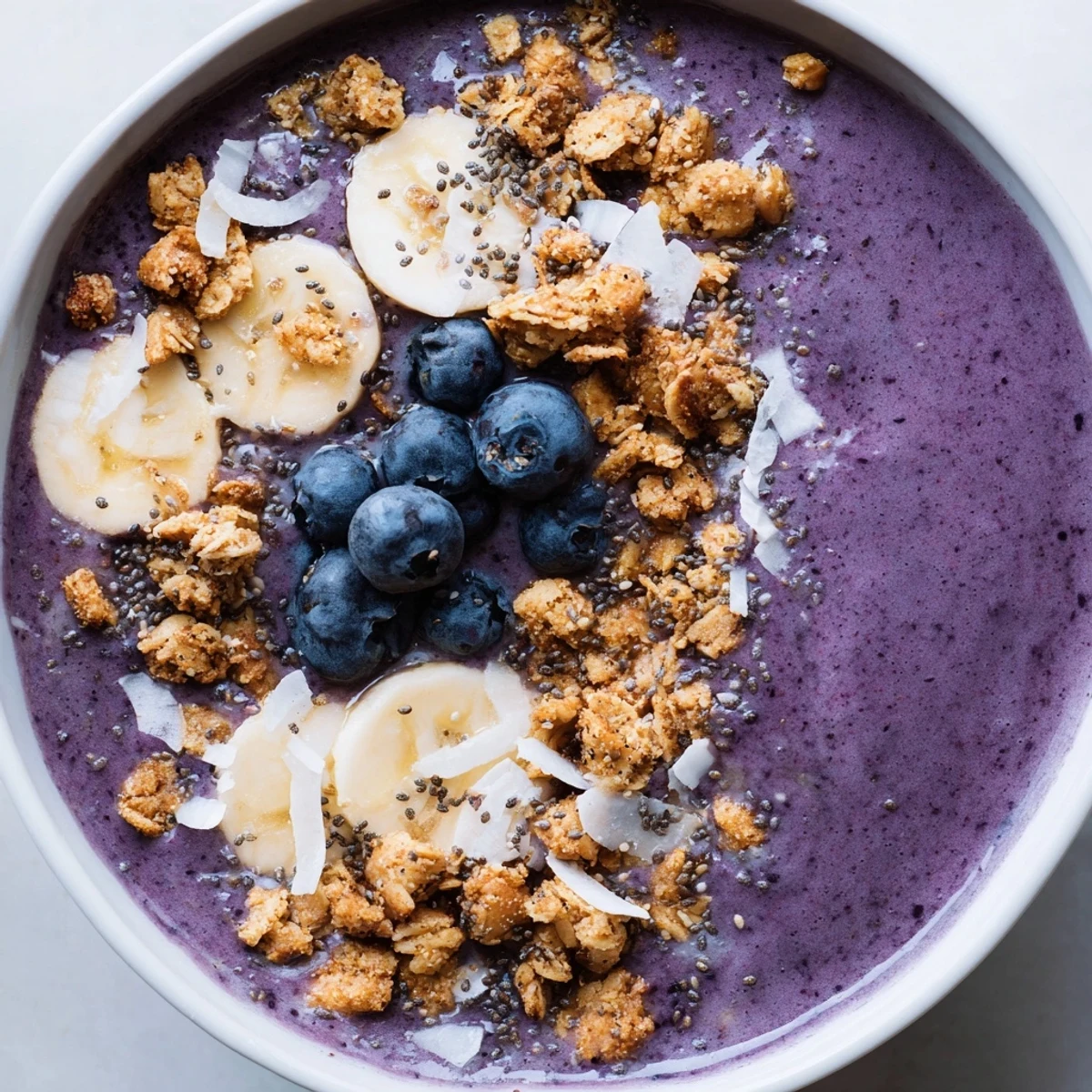 Vibrant purple blueberry coconut banana smoothie bowl garnished with coconut flakes and banana slices
