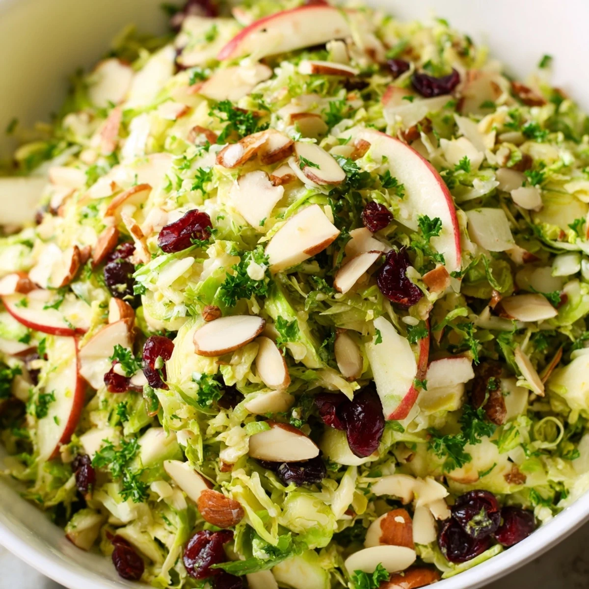 Crunchy Brussels sprout apple almond salad drizzled with sweet maple dressing in a wooden bowl
