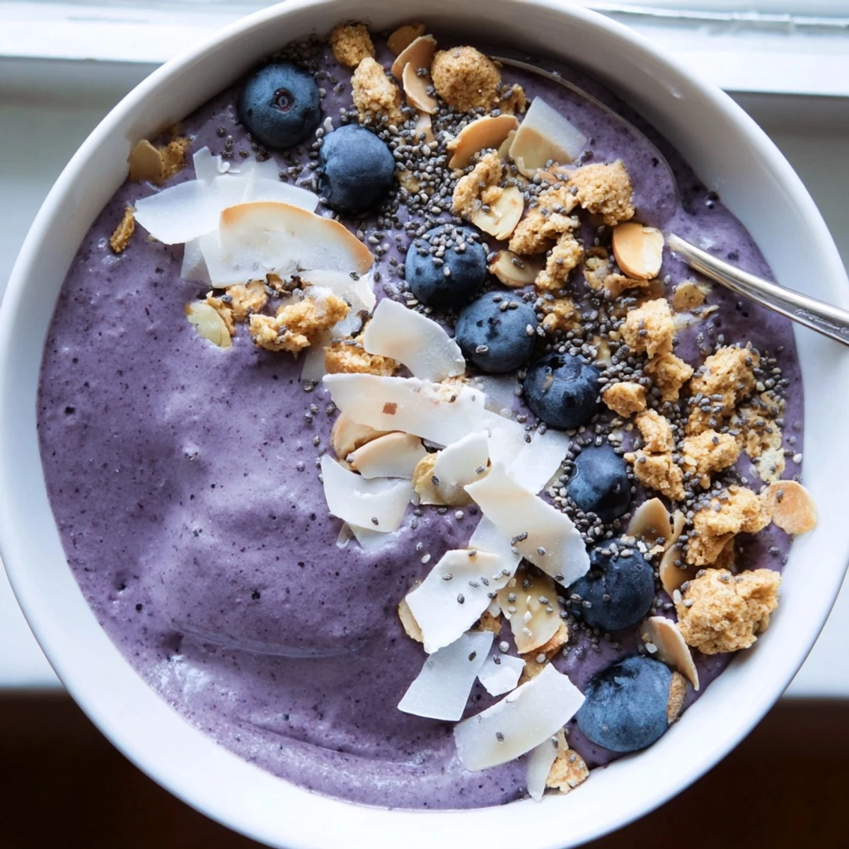 Creamy blueberry almond coconut smoothie bowl topped with crunchy granola and fresh berries