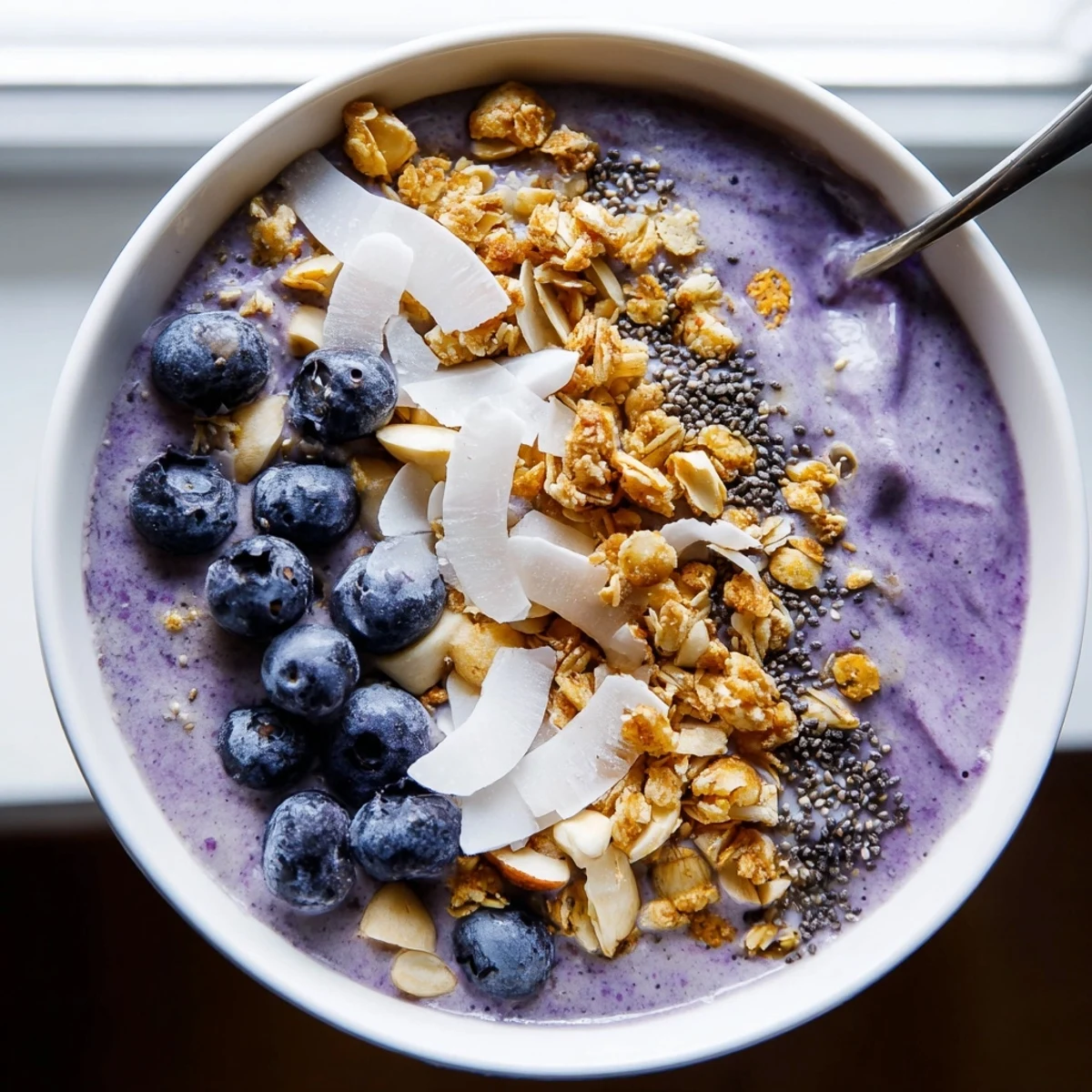 Vibrant purple blueberry almond coconut smoothie bowl crowned with shredded coconut and sliced almonds