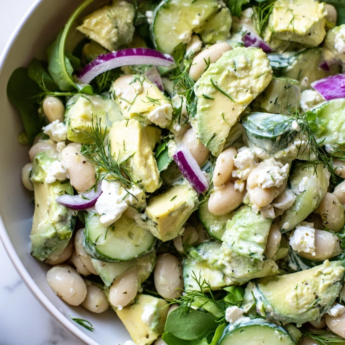 Creamy avocado cucumber white bean salad bowl topped with crumbled feta and fresh dill
