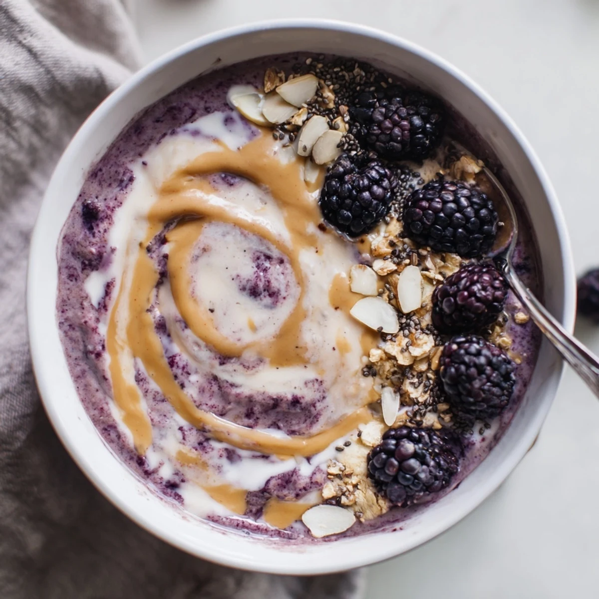 Blackberry Vanilla Oat Smoothie Bowl with Almond Butter Swirl, thick and spoonable, sliced almonds