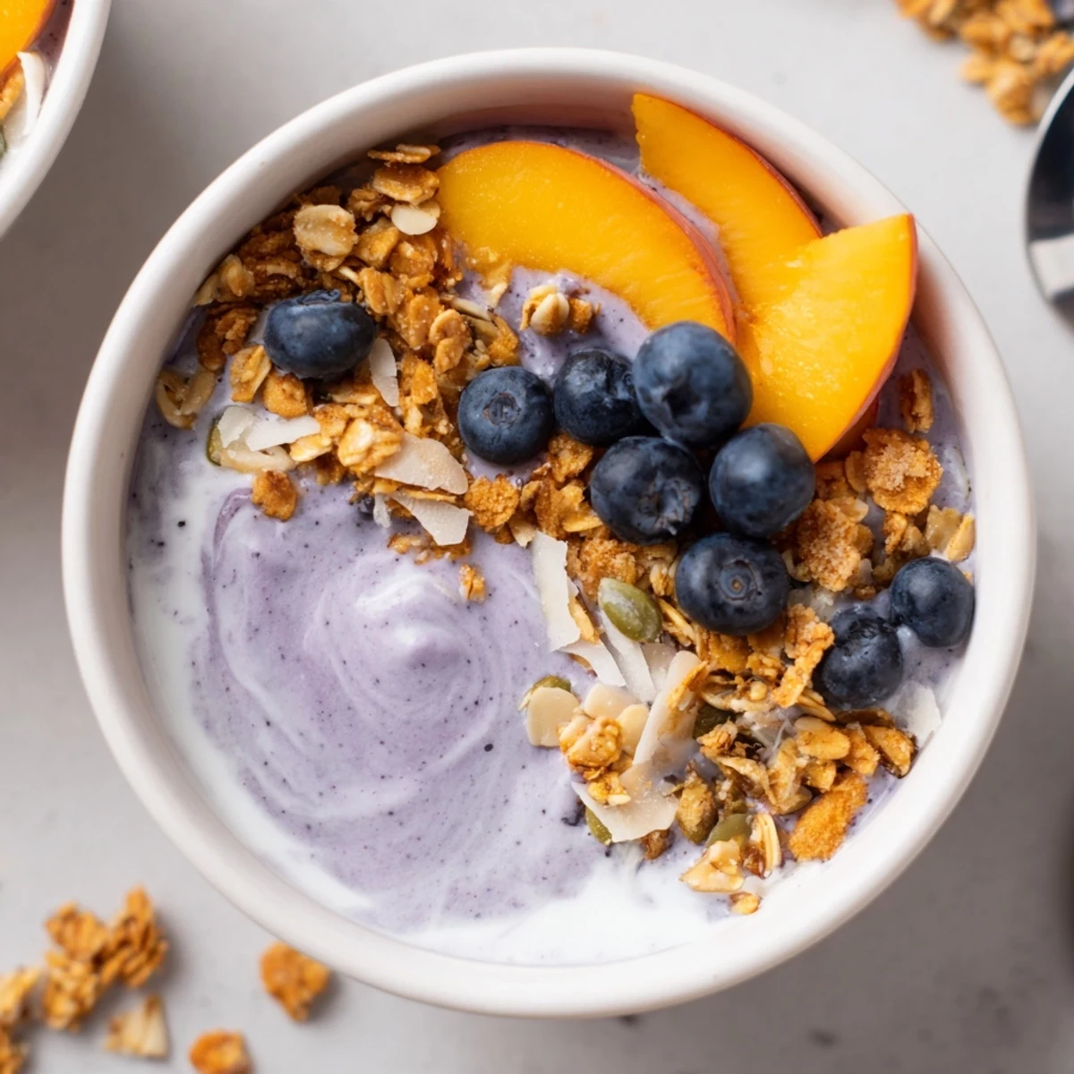 Frosty Blueberry Peach Coconut Smoothie Bowl with Granola Clusters, topped with fresh peach.