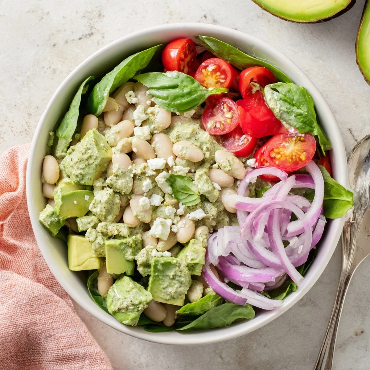 Colorful creamy avocado basil white bean salad bowl with juicy red cherry tomatoes and fresh greens