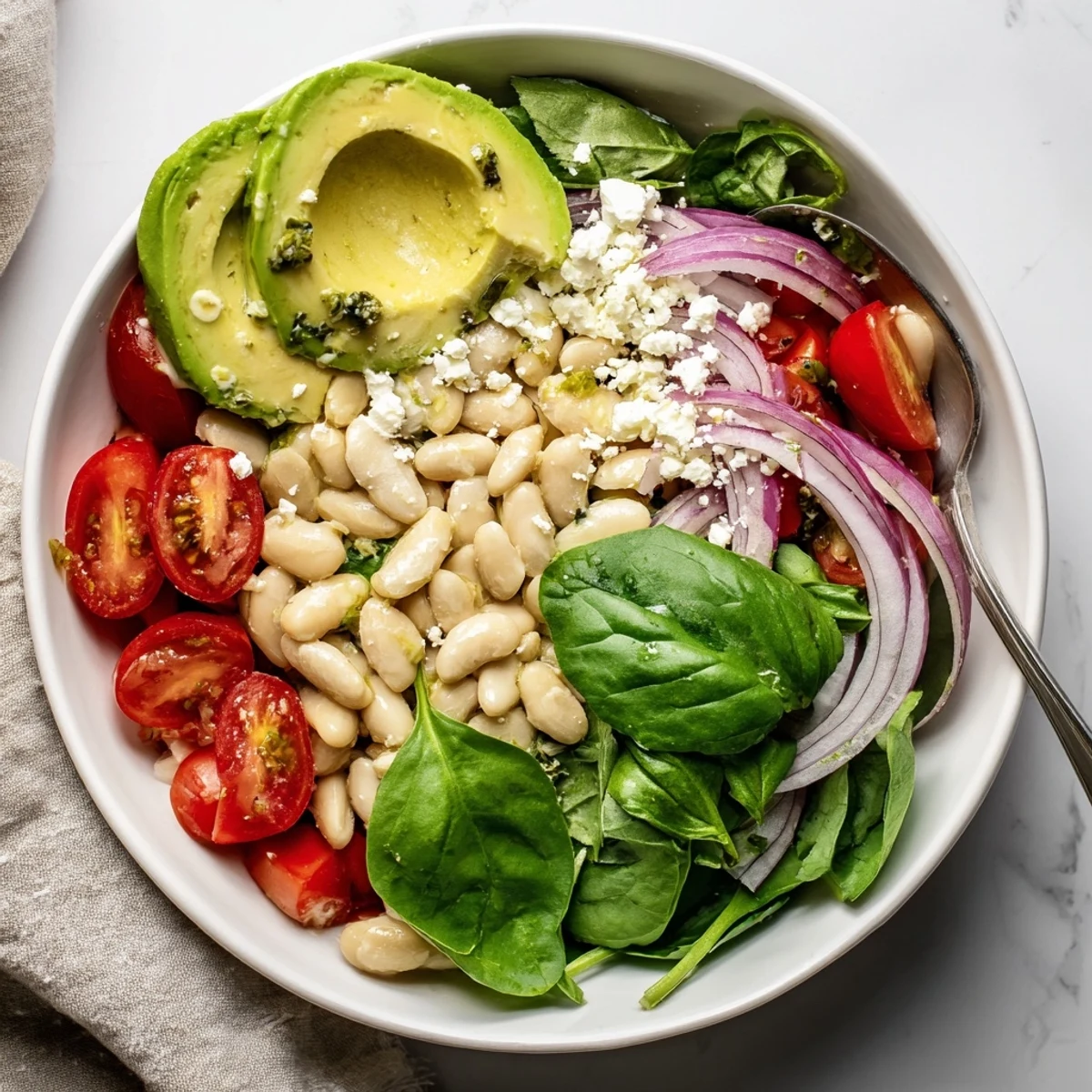 Hearty white bean salad bowl topped with ripe avocado slices and basil in bright sunlight