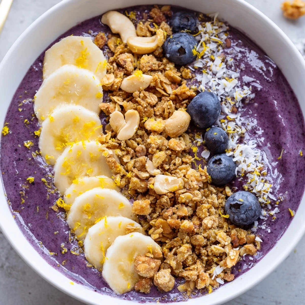 Creamy vibrant smoothie bowl with homemade granola crumble, fresh blueberries, banana slices, and cashew pieces