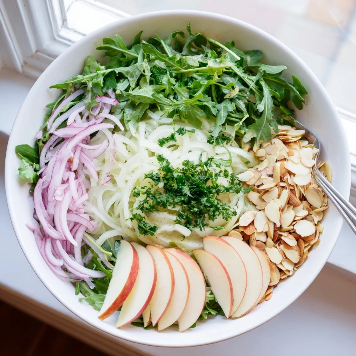 Colorful shaved fennel and apple salad bowl with toasted almonds drizzled with citrus vinaigrette