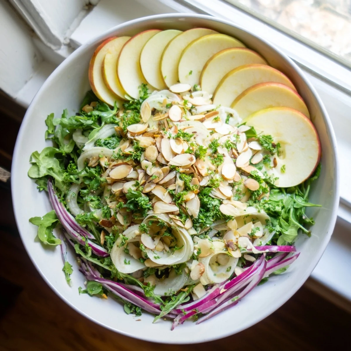Fresh fennel apple salad bowl topped with crunchy almonds and bright citrus dressing