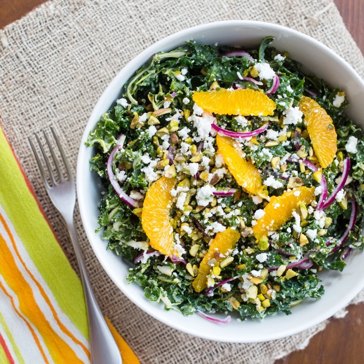 Vibrant shaved kale orange pistachio salad in white bowl featuring juicy citrus segments and crunchy nuts