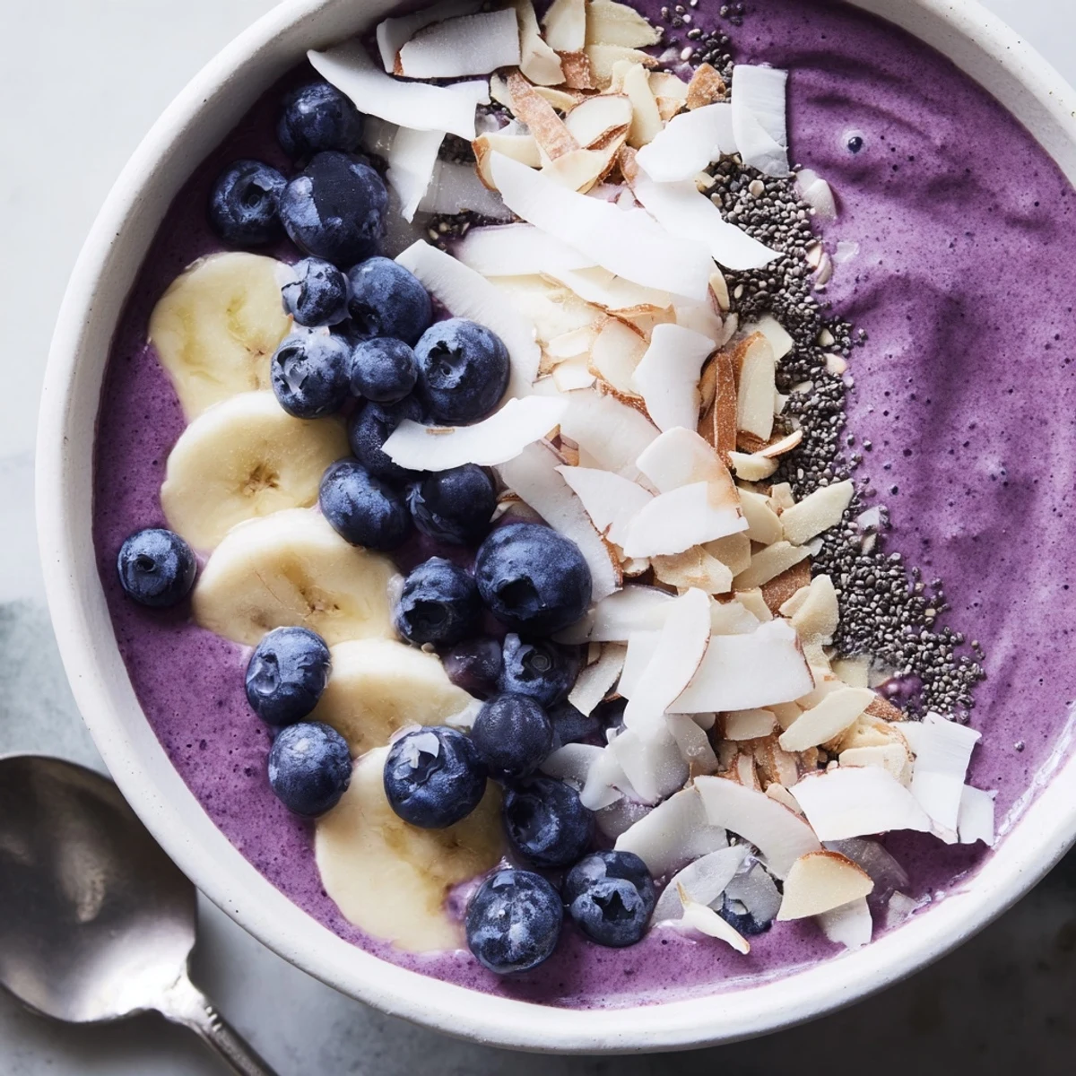 Vibrant blueberry banana almond smoothie bowl featuring sliced bananas and toasted coconut garnish
