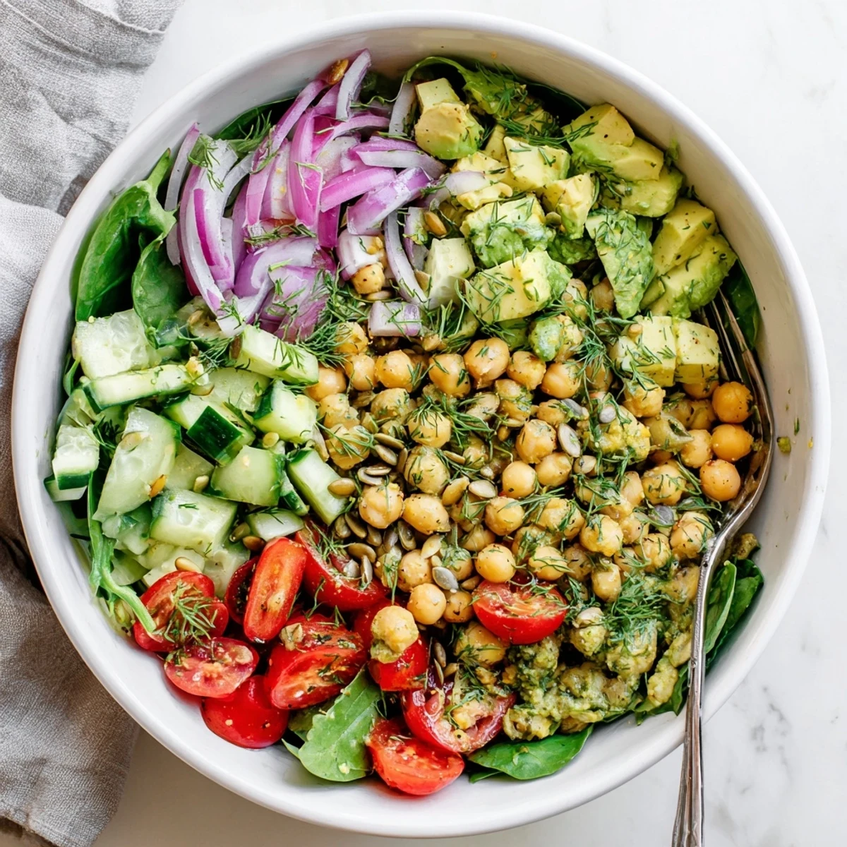 Colorful creamy avocado lemon chickpea salad bowl topped with fresh green dill