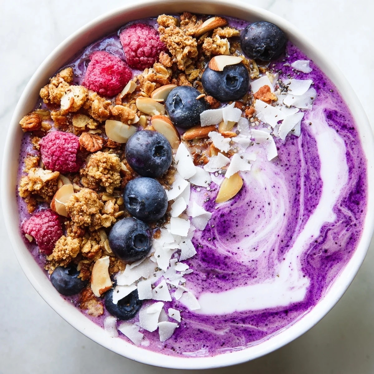 Vibrant blueberry raspberry coconut smoothie bowl topped with crunchy granola and fresh berries