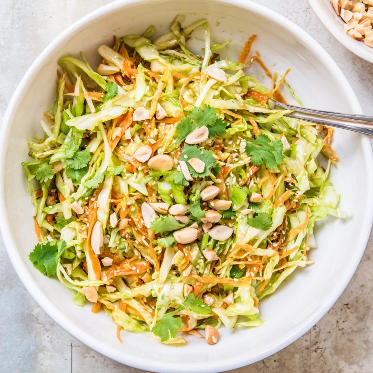 Vibrant shaved cabbage carrot almond salad bowl drizzled with creamy sesame dressing and topped with crunchy toasted nuts