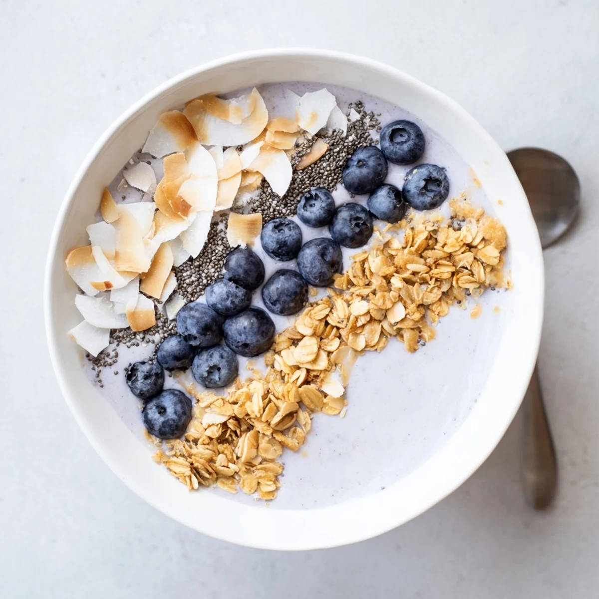 Blueberry Almond Coconut Smoothie Bowl with Granola Clusters, creamy purple swirl topped with coconut