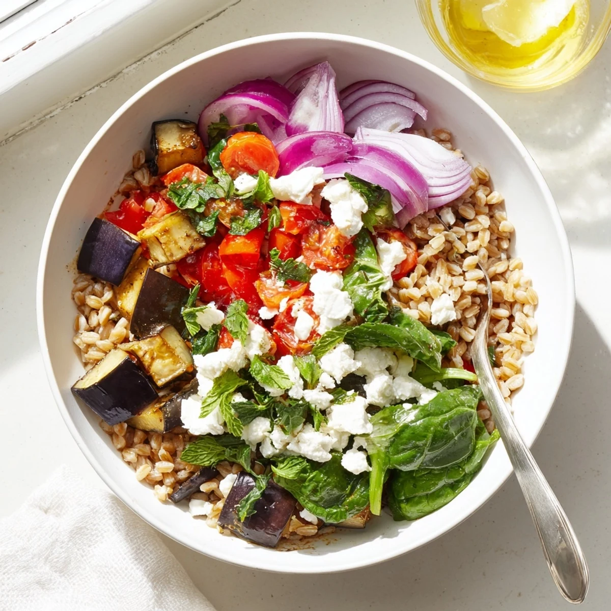 Golden roasted eggplant and vegetables tossed with fluffy farro in a colorful Mediterranean grain bowl topped with creamy feta cheese