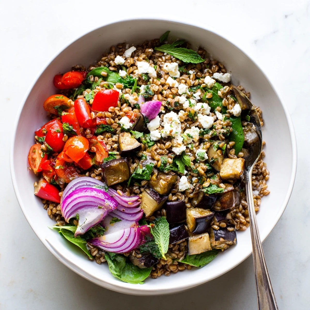 Hearty farro grain bowl with roasted eggplant, juicy cherry tomatoes, red peppers, and crumbled feta dressed with lemon and herbs