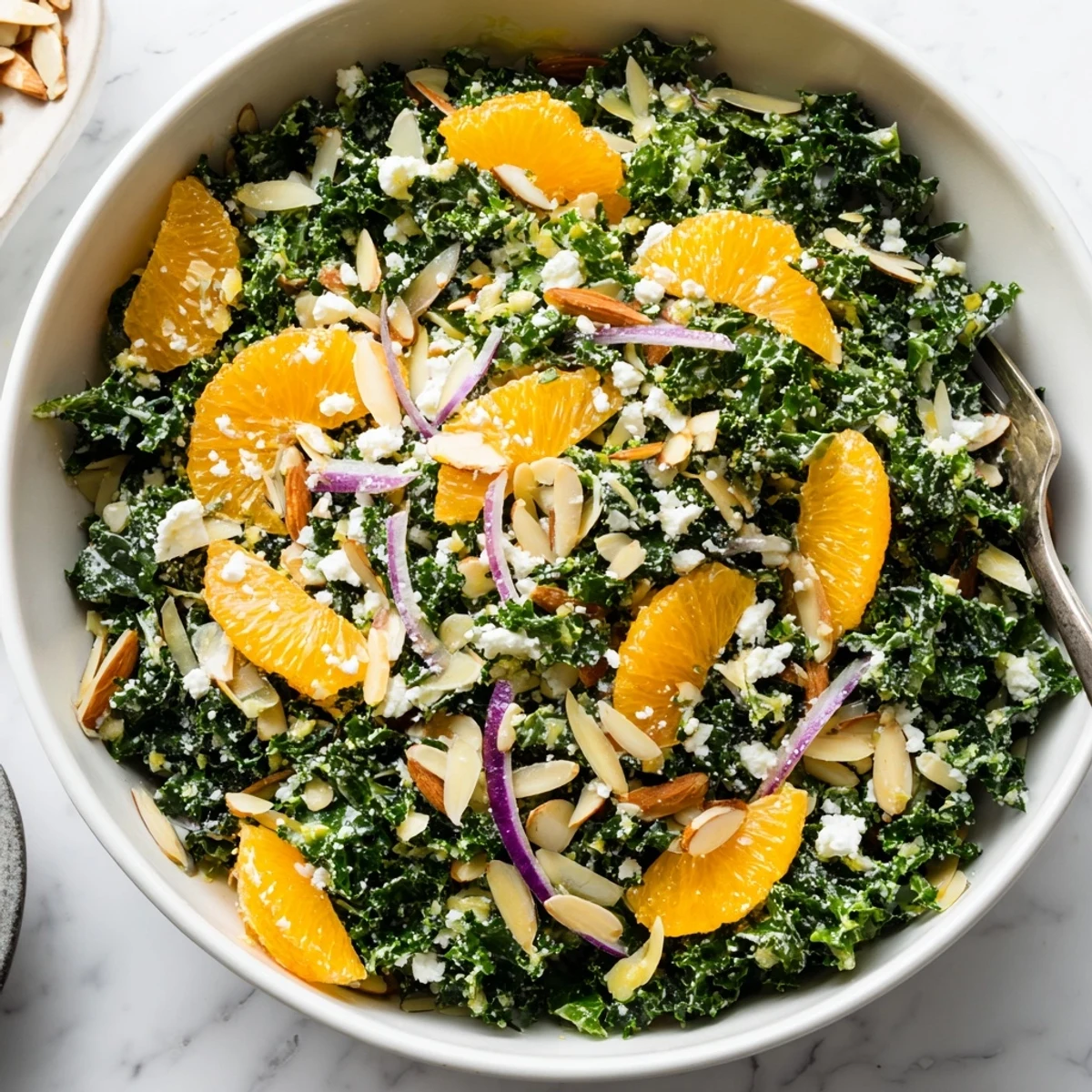 Fresh shaved kale orange almond salad bowl topped with toasted almonds and zesty citrus dressing