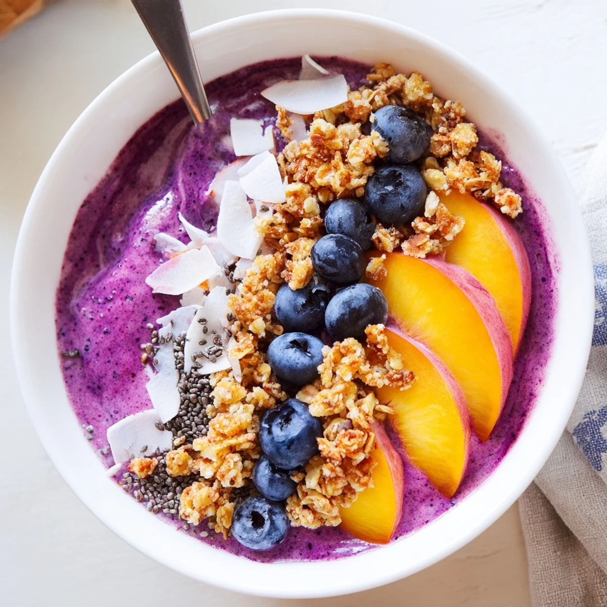 Vibrant breakfast bowl with blended blueberries, peaches, and coconut milk under granola topping